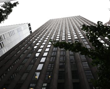 A tall building soaring toward the sky and viewed from the street.