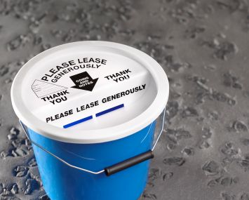 Charity collection bucket that read "Please Lease Generously."